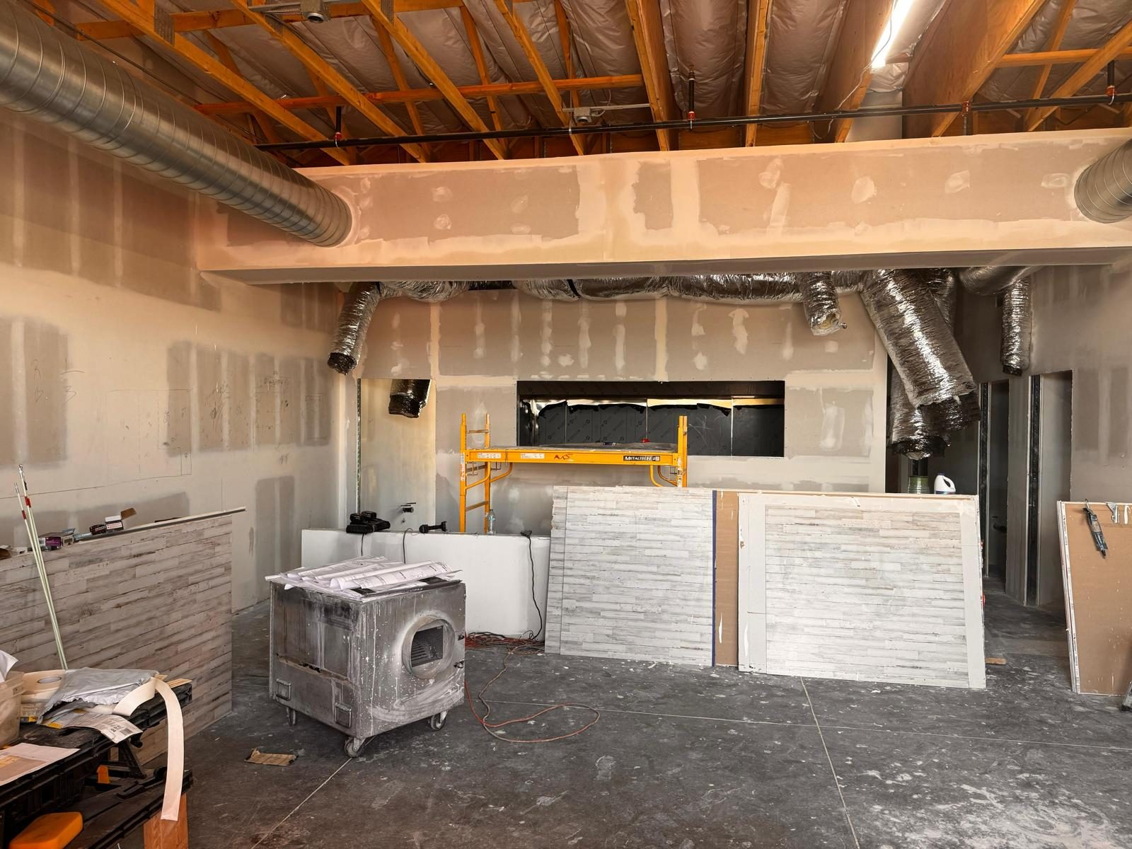 Front counter framed with stacked-stone panels and scaffold at the kitchen pass-through