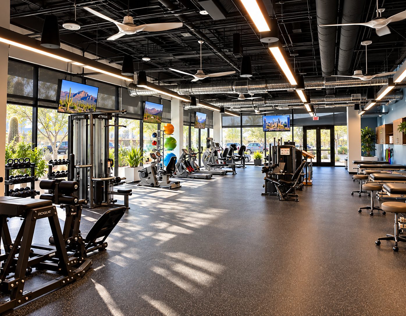Open floor with strength machines, a cardio row along the glass and treatment tables at right