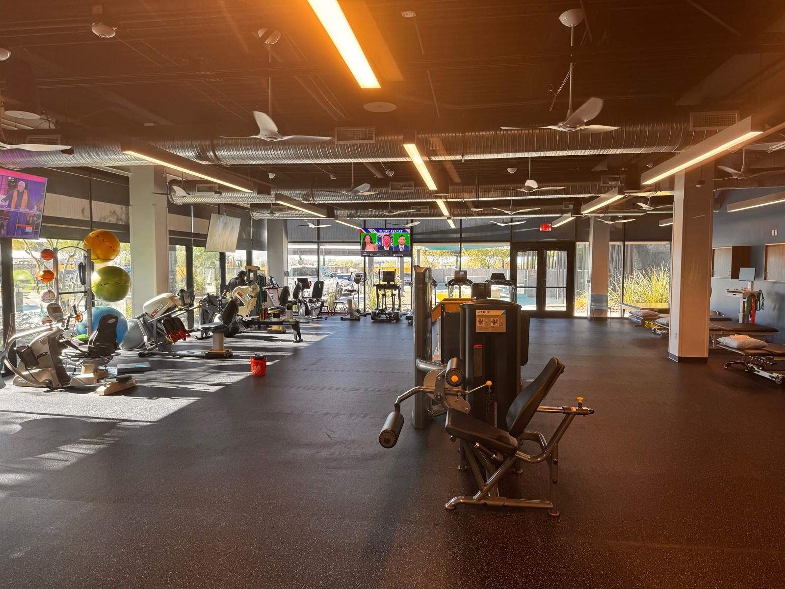 Open therapy floor with strength equipment, cardio row and treatment tables